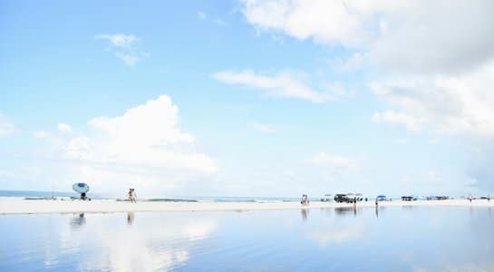 Calm scene at Grayton Beach, Florida, with the blue sky reflected in a shallow tidal pool and a few beachgoers in the distance—great for RV camping trips File name: grayton-beach-best-florida-state-parks-for-rv-camping-545x300.jpg