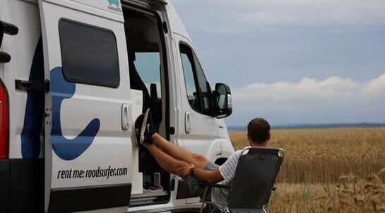 Guy sitting on his camping chair in front of a Fiat Ducato campervan in the middle of a field