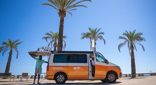 two guys loading their campervan from roadsurfer standing at a beach with palm trees