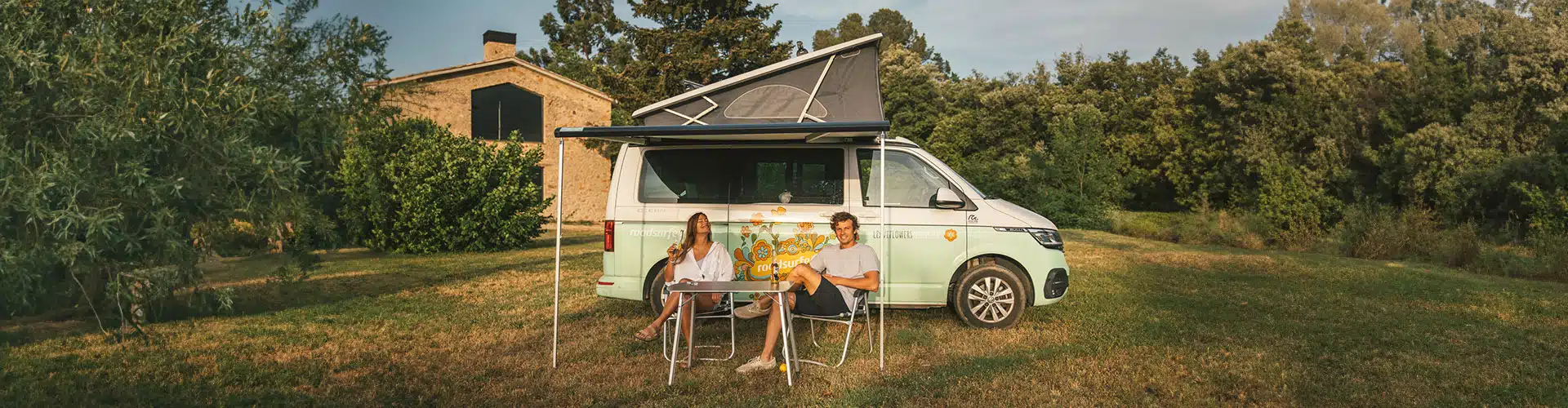 Happy couple with drinks sitting in front of a campervan