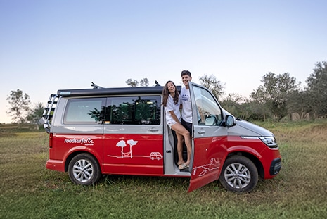 Happy couple posing while leaning out of a parked roadsurfer campervan in a field