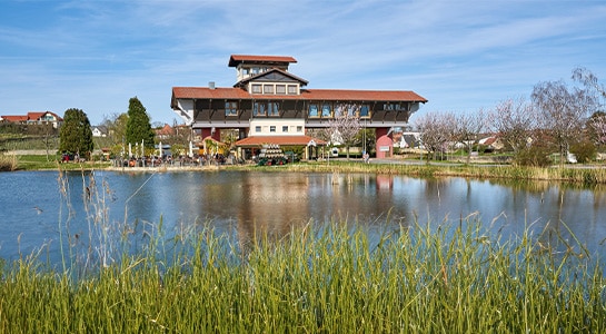 Brown house at the like with green grass surrounding it and an almost clear blue sky.