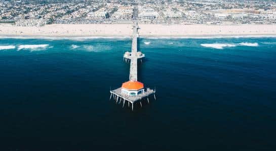 Aerial view of Huntington Beach Pier stretching into the Pacific Ocean with the coastline in the background