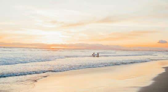 Surfers catching waves during a golden sunset at Huntington Beach, a classic destination for beaches in LA.
