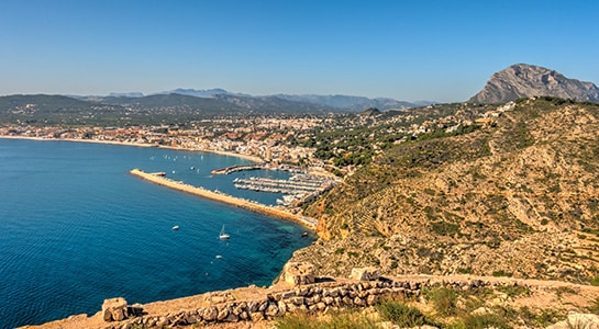 Aerial view of Jávea on Spain’s Costa Blanca, with the Mediterranean Sea, marina, rugged coastline and mountains in the background.