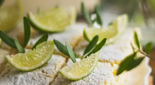 Key lime dessert squares topped with powdered sugar and lime wedges on a wooden board.