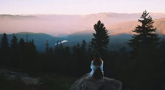 Visitor sitting on a rock overlooking mountain valleys in Kings Canyon National Park