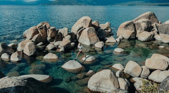 Hiker hopping across granite boulders over clear turquoise water at Lake Tahoe—fun things to do in Northern California with kids.