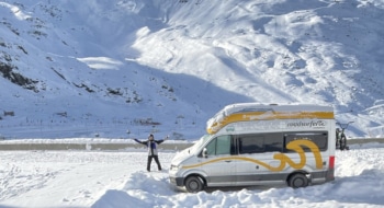 man next to a campervan in the snow waving to the camera
