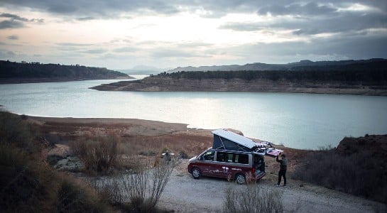 man closing the trunk of a campervan parked next to a lake