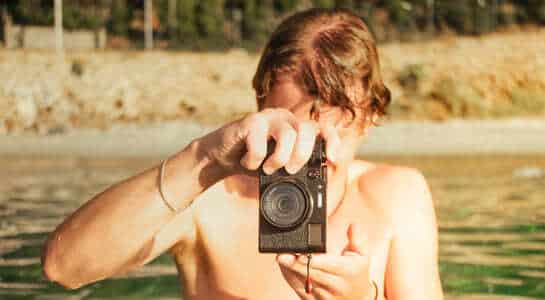 Man holding camera like he is photographing someone, while being in water.