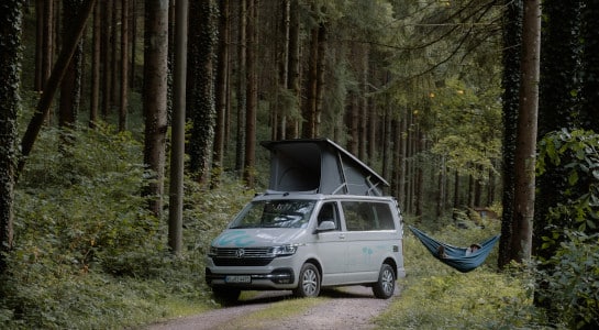 man in a hammock next to a camper van in a forest