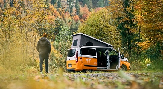 man next to a yellow camper van in an autumn landscape