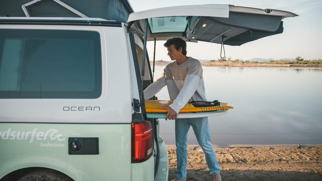 man putting surfboards in the back of a campervan