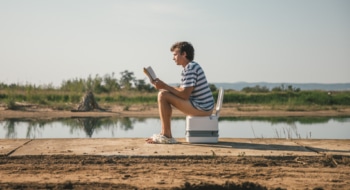 Man reading a book on a porta poti toilet in the wilderness