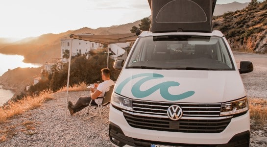 man sitting in a chair in front of his campervan looking at the sea