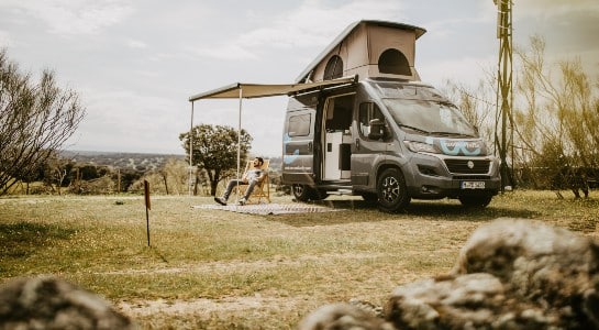 man sitting in a chair on a lawn next to a campervan with open roof