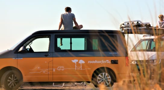 man sitting on top of a yellow campervan