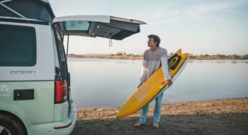 man with yellow surfboard and campervan