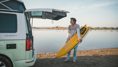 man with yellow surfboard and campervan