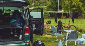 Two men siting on a campsite next to their parked campervan.