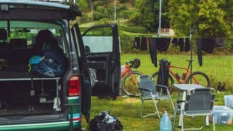 Two men siting on a campsite next to their parked campervan.