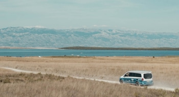 Mercedes Marco Polo camper van from roadsurfer driving down a dirt road towards a lake and mountains