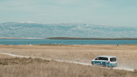 Mercedes Marco Polo camper van from roadsurfer driving down a dirt road towards a lake and mountains