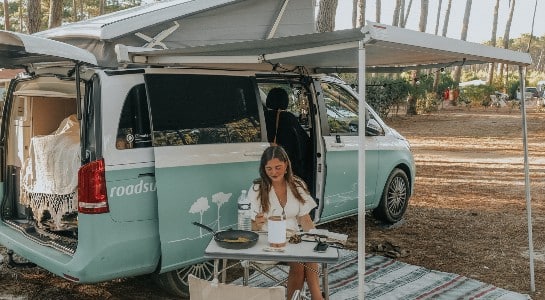 Girl having lunch under the awning of a turquoise Mercedes Vito
