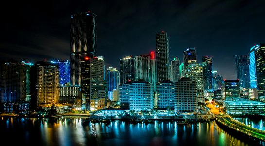 Night view of the Miami skyline with colorful lights reflecting on the calm waters of Biscayne Bay.