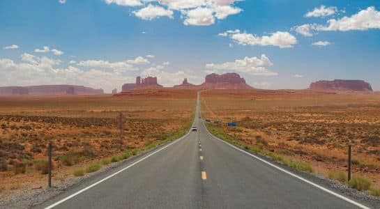 Driving Route 66 on a long straight desert highway toward Monument Valley rock formations