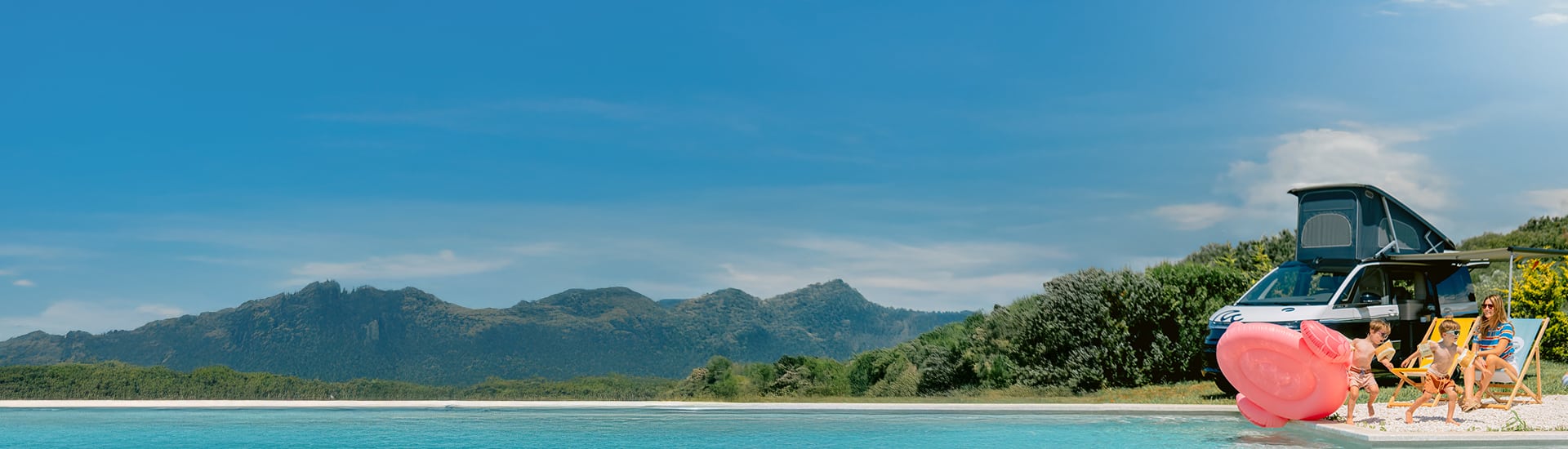 Mother with two kids relaxing next to a pool with a parked campervan in the background