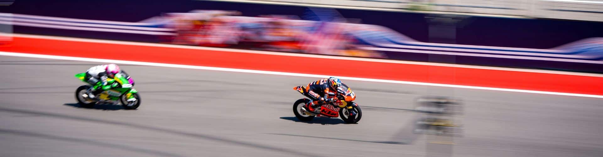 Multiple MotoGP bikes speeding along a racetrack with motion blur showing high racing intensity