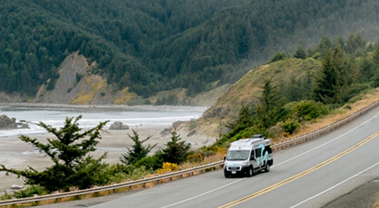 motorhome on the road in front of a river with rocks and trees