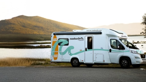 Motorhome parked near a scenic lake with a mountain in the background, bathed in warm sunlight