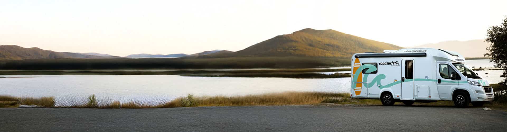 Motorhome parked near a scenic lake with a mountain in the background, bathed in warm sunlight