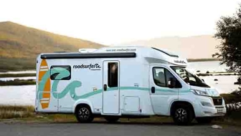 Motorhome parked near a scenic lake with a mountain in the background, bathed in warm sunlight