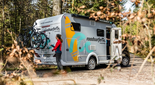 Woman putting two bikes on the bike carrier of a motorhome standing in a forest