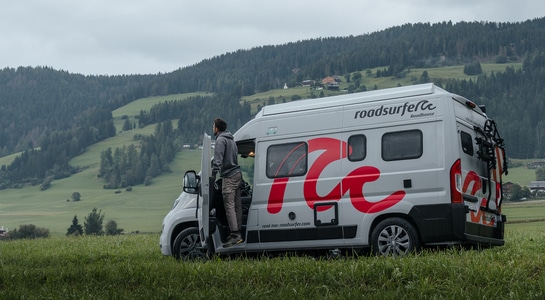 roadsurfer motorhome standing on a field road of Switzerland with the driver standing on the door step