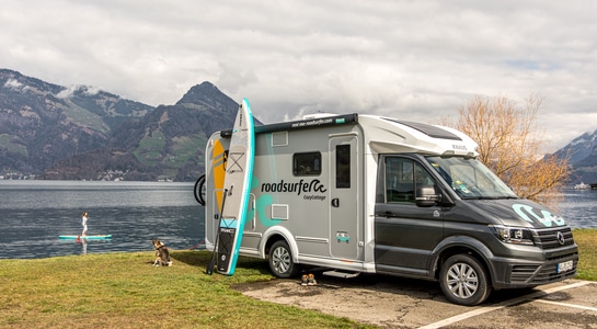 motorhome standing next to a lake with a paddle surf leaned on the vehicle