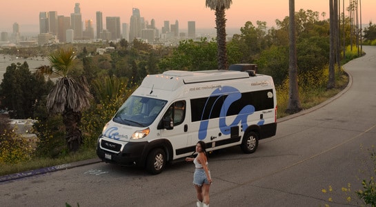 roadsurfer motorhome standing on a hill with the sunset over Los Angeles in the horizon