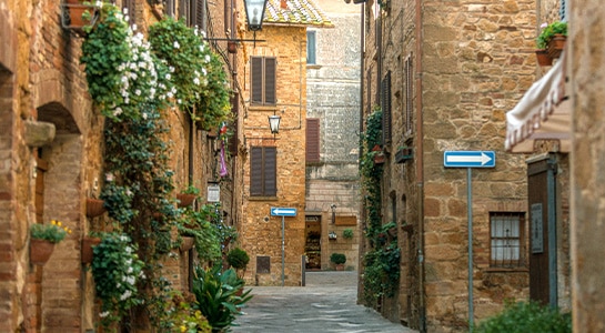 Narrow alley way between orange-ish houses in the city of Pienza.