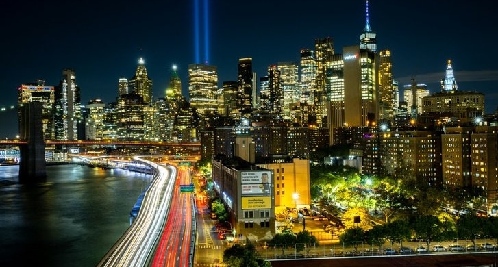 Night view of New York City skyline with Tribute in Light beams and traffic light trails along the river