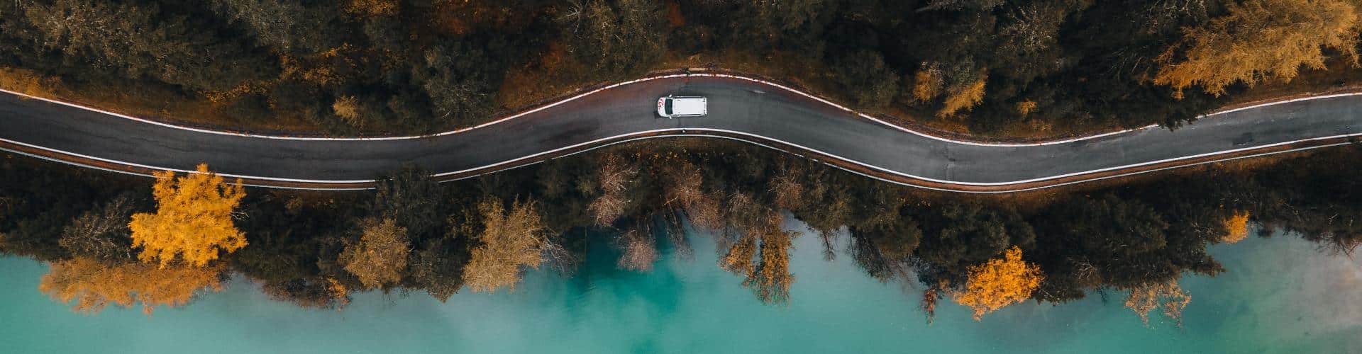 One-way RV rental driving along a road beside a calm lake and forest landscape