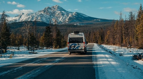One-way RV rental driving along a snowy mountain road with forest scenery