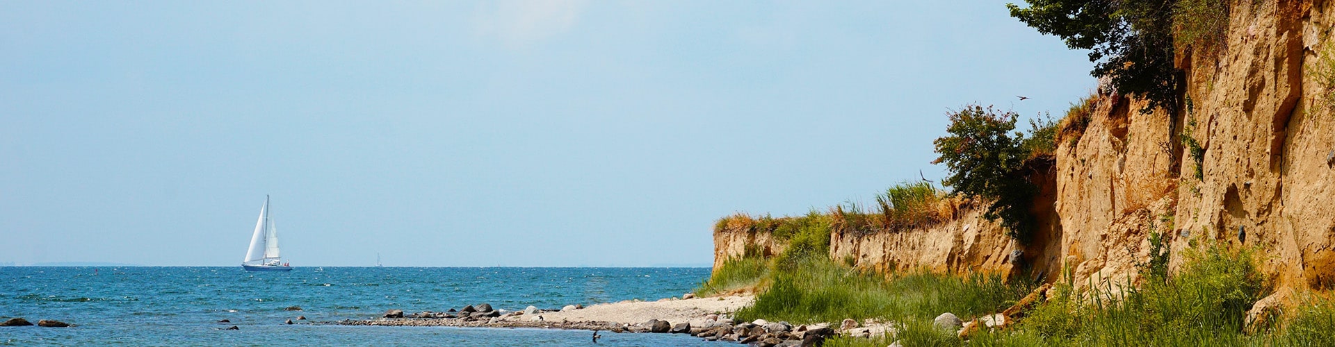 Rocky cliffs at the edge of the Baltic Sea and a sailboat visible in the background.