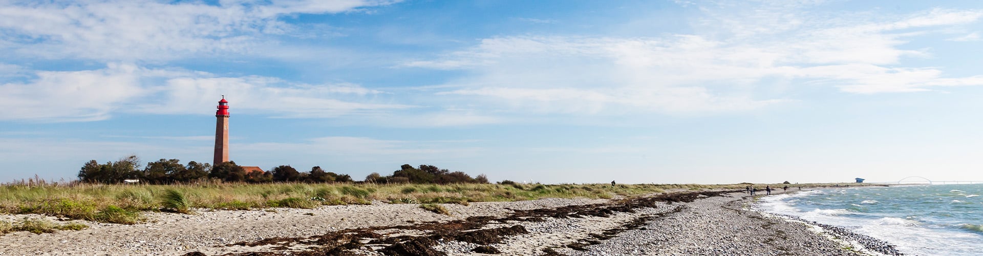 Pebble beach with the sea to the right side and a red light house to the left.