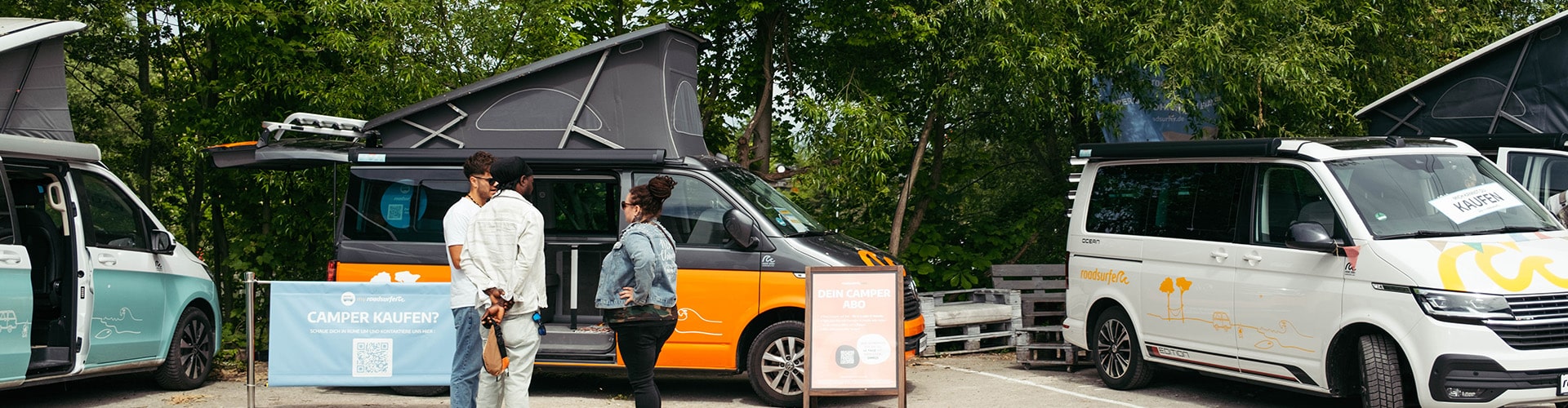 People being advised by sales manager on roadsurfer sales day, while standing in between different campervans.