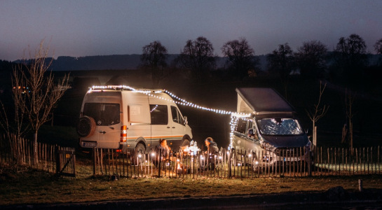People sitting around a campfire between two campervans with fairy lights