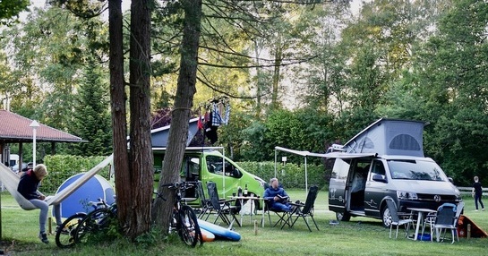 Campervans parked on a campsite and people sitting around tables.